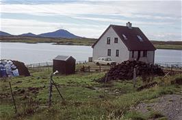 This resident at Blathaisbhal, two miles out of Lochmaddy, has collected a good store of peat bricks for winter fuel.  This view looks back over Lochmaddy to one of North Uist's big mountains, Eaval, 347m [New photo, July 2019]