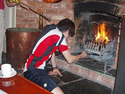 Keir tends the fire; Osian menaces him with the tongs.