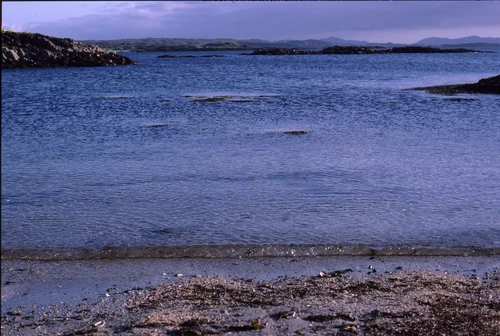 Camusdarach's crystal water and skerries, with Rum and Eigg faint beyond.