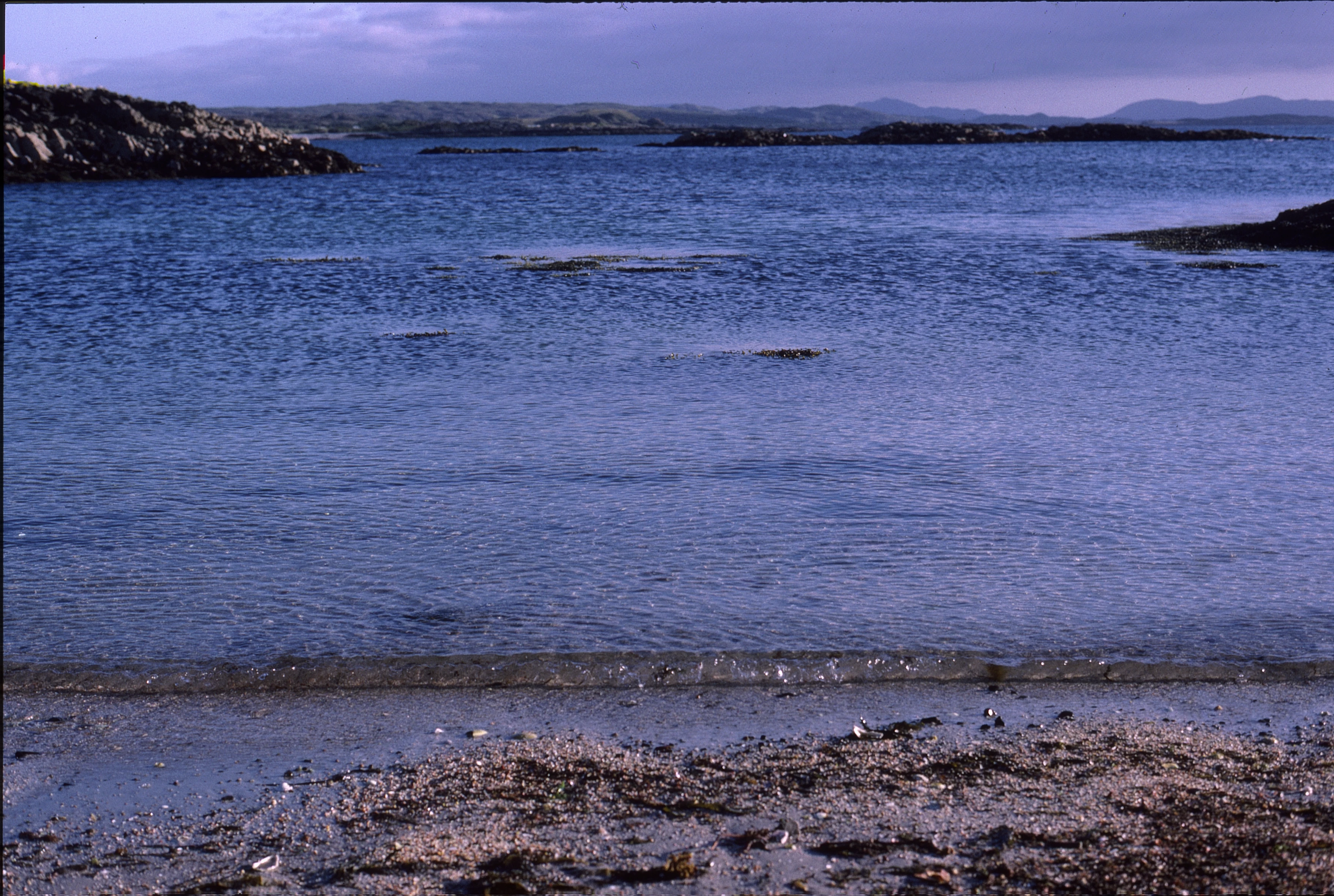 Camusdarach's crystal water and skerries, with Rum and Eigg faint beyond.