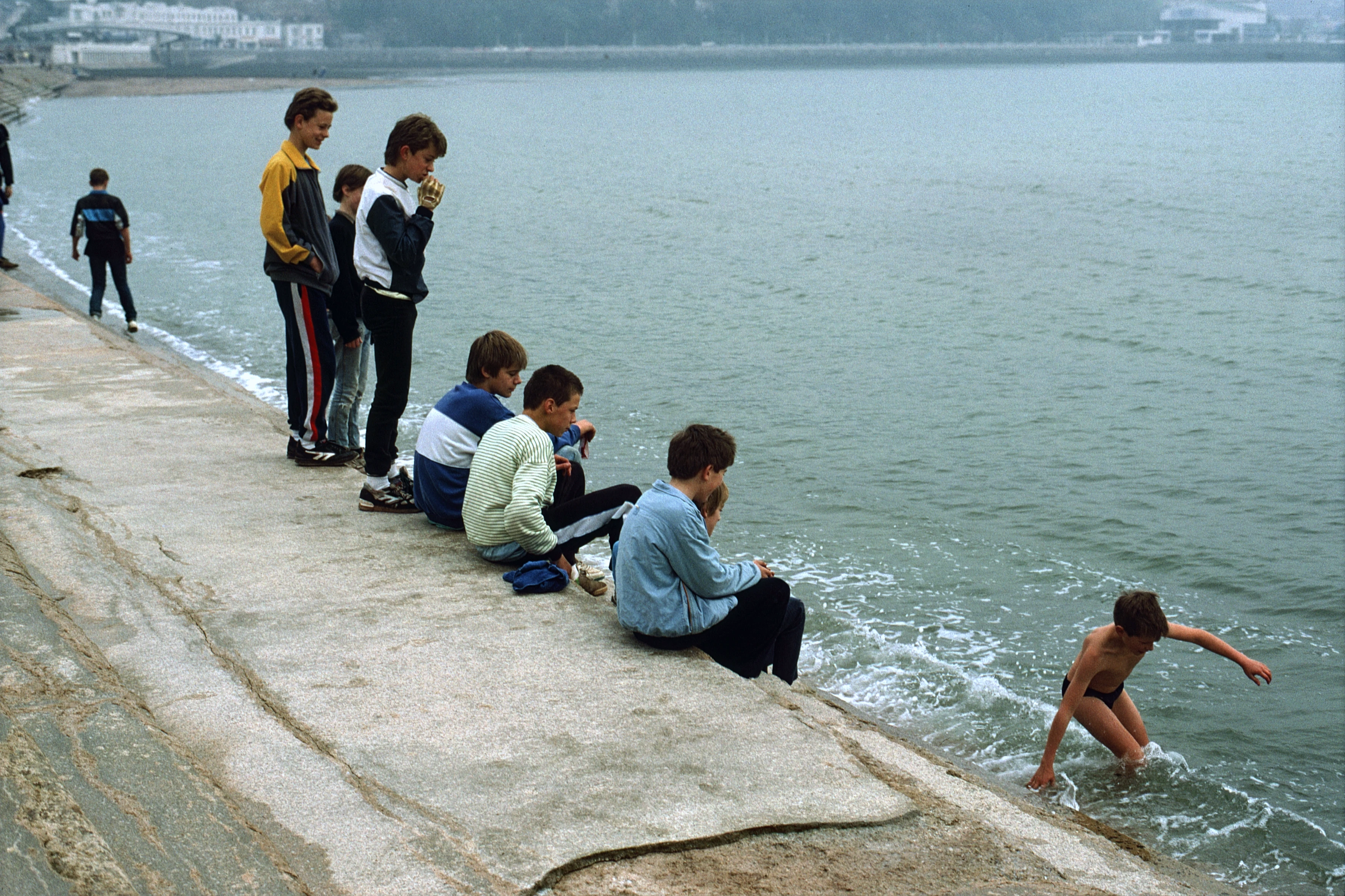 Jonathon wades into the icy sea below Torquay promenade while the rest of the group stay dry above, entertained.
